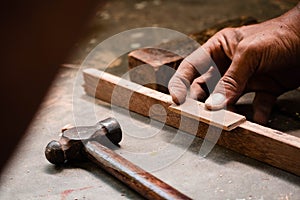A mechanic does carpenter jobs with wood, plus and other tools. He is hitting hammer on the head of nail to wooden pieces and