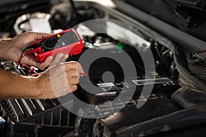 Mechanic doing car inspection, he is testing car battery with tester. Check battery voltage with electric multimeter