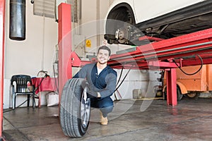 Mechanic Examining Car Tire While Crouching In Workshop