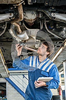Mechanic Examining Exhaust System Of Car With Flashlight