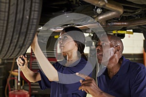 Mechanic And Female Trainee Working Underneath Car Together