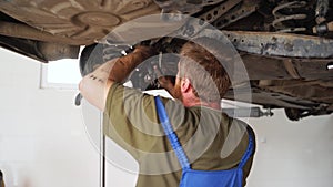 Mechanic fixes car suspension in garage, using wrench under lifted vehicle. Auto repair, wheel alignment, maintenance