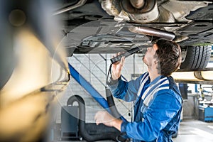 Mechanic With Flashlight Examining Under The Car