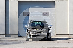 Mechanic garage entrance with closed doors and grey family car with ripped apart front left outside waiting for new parts