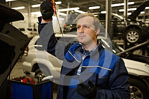 Mechanic in garage examining the car engine oil dipstick checking motor oil level at a car. Car engineer technician in the car