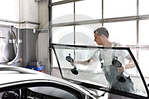 Mechanic in a garage replaces defective windshield of a car