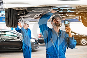 Mechanic and his assistant examining the car bottom with flash light. Auto car repair service center. Professional service