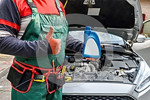 Mechanic holding bottles with oil near car engine