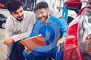 Mechanic holding clipboard with car owner in the workshop garage. Car auto services concepts