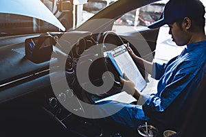 Mechanic holding clipboard and checking inside car to maintenance vehicle by customer claim order in auto repair shop garage.