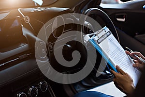 Mechanic holding clipboard and checking inside car to maintenance vehicle by customer claim order in auto repair shop garage.