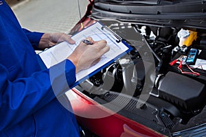 Mechanic holding clipboard in front of open car engine