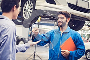 Mechanic holding clipboard giving the key back to car owner in the workshop garage. Car auto services concepts