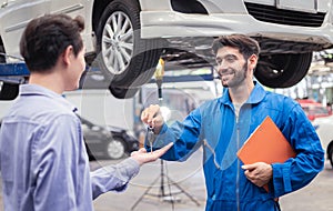 Mechanic holding clipboard giving the key back to car owner in the workshop garage. Car auto services concepts