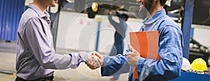 Mechanic holding clipboard shaking hands with car owner in the workshop garage. Car auto services concepts