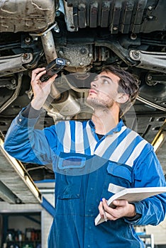 Mechanic Holding Flashlight While Examining Car Exhaust System