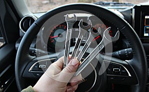 A mechanic holds a bunch of wrenches in front of the steering wheel and blurred dashboard in car with the ignition on