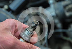 a mechanic holds a car engine spark plug in his hand