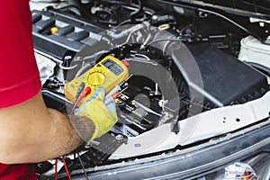 A mechanic holds a digital multimeter to check the car electrical system