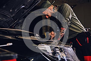 Mechanic inspecting car`s engine in a workshop.