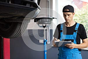Mechanic inspects the car undercarriage way and makes a note on his inspection sheet. Car service employe inspect car
