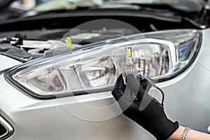 mechanic installing modern led H7 light bulb with wires in headlamp