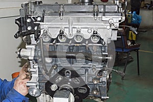 A mechanic installs a pulley on the crankshaft of an automobile engine mounted on an engine repair stand