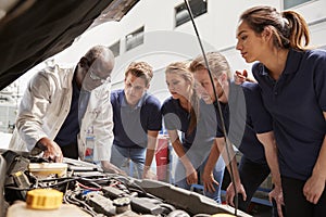 Mechanic instructing trainees around a car engine, low angle