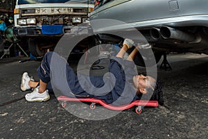 Mechanic lying down and working under car at auto service garage. Technician vehicle maintenance and checking under car at automot