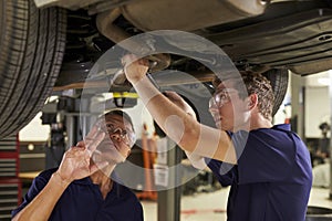 Mechanic And Male Trainee Working Underneath Car Together