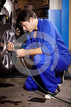 Mechanic, man and change wheel in shop, electric drill and car service or auto repairs for maintenance. Technician, male