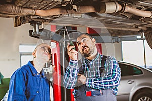 Mechanic man examining car with trainee girl