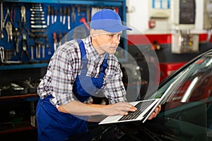 Mechanic man with laptop making car diagnostics at service