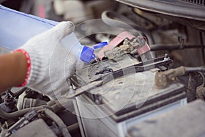 Mechanic man pouring distilled water to fill car battery in automobile engine at repair service workshop garage, close up
