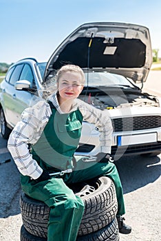 Mechanic posing with tyres on roadside with car.