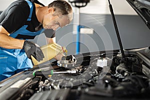 The mechanic is pouring oil into the engine. Pouring fresh oil to car engine, oil change to auto. Caucasian man in blue