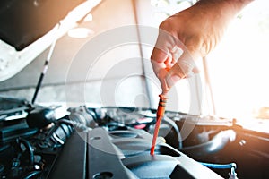 The mechanic is pulling the dipstick in the engine compartment to check the oil level