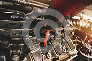 A mechanic is pulling the orange dipstick to check the oil level of the combustion engine