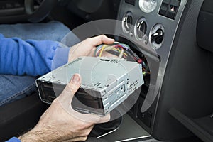A mechanic puts a car audio into a car radio pocket. Connecting the radio.