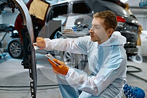 Mechanic puttying plastering car body in garage