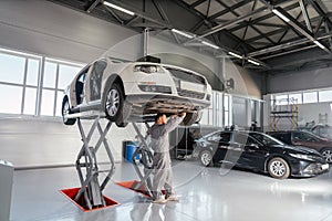 Mechanic repairing Car on lift in mechanic shop or garage, interior of auto repair workshop