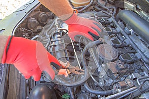 The mechanic is repairing the car. The mechanic`s hands on the background of the open bonnet repairs the details