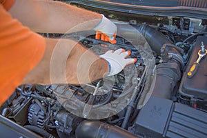 The mechanic is repairing the car. The mechanic`s hands on the background of the open bonnet repairs the details