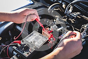 Mechanic repairman checking engine automotive in auto repair service and using digital multimeter testing battery to measure