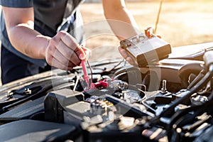 Mechanic repairman checking engine automotive in auto repair service and using digital multimeter testing battery to measure