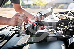 Mechanic repairman checking engine automotive in auto repair service and using digital multimeter testing battery to measure