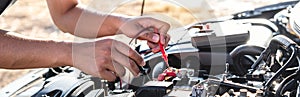 Mechanic repairman checking engine automotive in auto repair service and using digital multimeter testing battery to measure