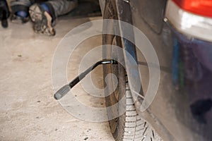 A mechanic repairs a car chassis. A man removes car wheels using a pneumatic screwdriver