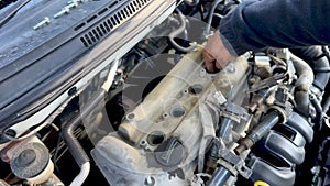 Mechanic's hand tightens nut on newly installed ignition coil on a car engine