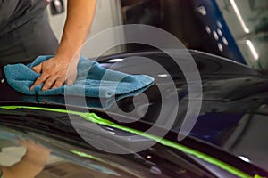 The mechanic in the service station polishes the car body, wiping with a napkin a glossy, shiny, clean, wax-coated black hood aft